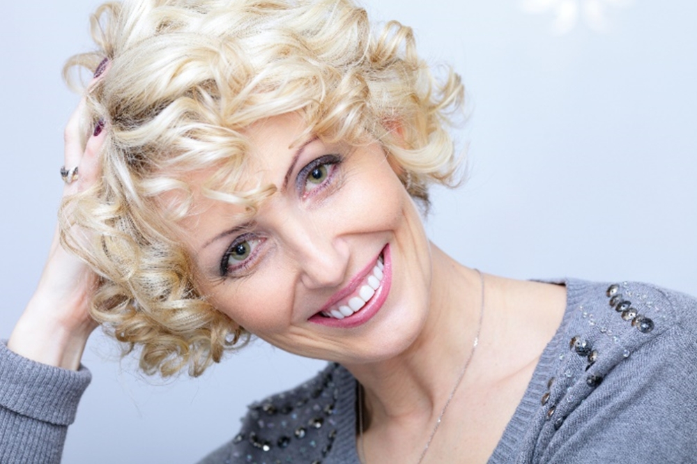 Žena v menopauze s krásnymi blond vlnitými vlasmi sa usmieva, pretože má dobrú kvalitu vlasov.