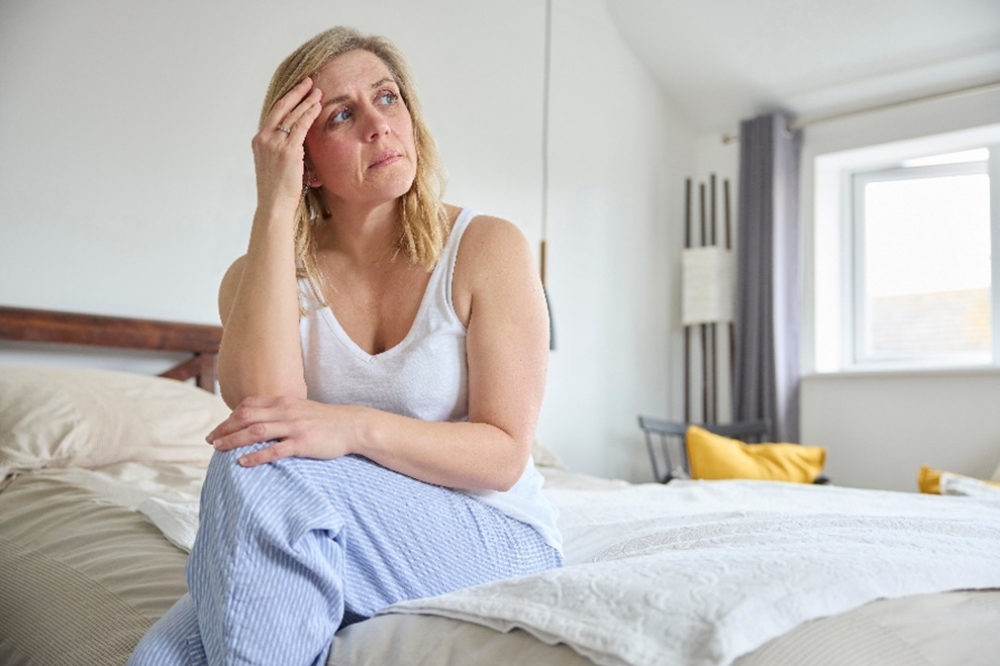 Žena sedí na posteli a trápi sa s otázkami o menopauze.